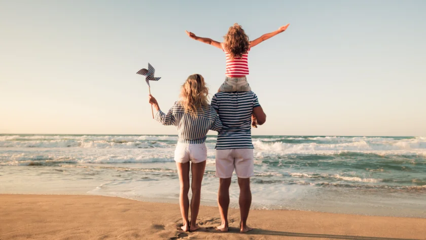 Family enjoying a sunny beach day, with child on dad's shoulders, capturing seaside bliss and playful moments by the waves.